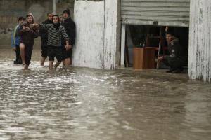A man looks out of his shop as Palestinians walk through a flooded road following heavy rain in Gaza City November 27, 2014. MOHAMMED SALEM/REUTERS