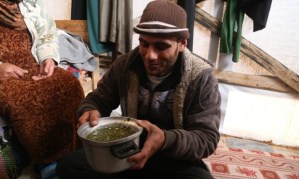 Baby Salma’s uncle with the wild grass soup that makes up the majority of the family’s diet Photograph: Belal Hasna