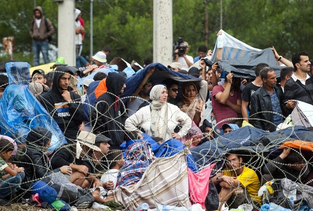 Refugees and migrants shelter from the rain as they wait in no-man's land along the Macedonian-Greek border near the town of Gevgelija, on August 22, 2015. Some 2,000 mostly-Syrian refugees spent a rainy night stranded in no-man's land between Greece and Macedonia as hundreds more began arriving on August 22, on their way to western Europe. The refugees and migrants, who have been there since August 20 spent the night sleeping on the ground despite heavy rain and temperatures which fell sharply during the night. Army troops were deployed throughout the forested hills which line the 50-kilometre (30-mile) border, army spokesman colonel Mirce Gjorgoski told AFP, giving no further details.  AFP PHOTO /ROBERT ATANASOVSKI